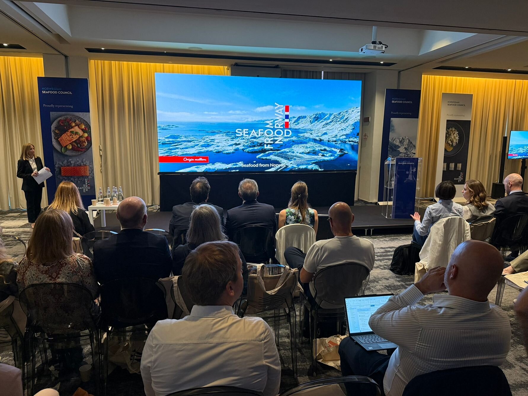 Publikum i sal og scene med presentasjon under sjømatseminar i Italia.