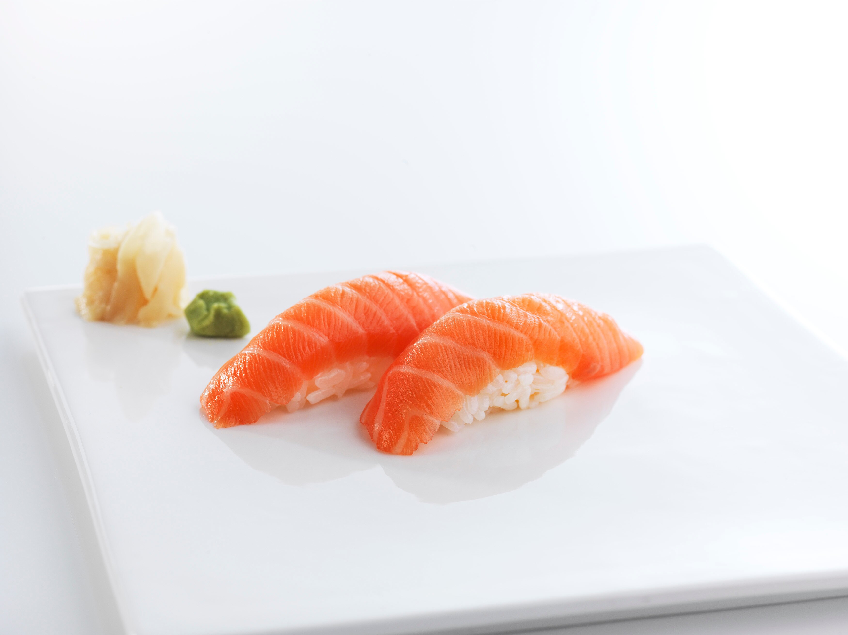 To biter med nigiri av norsk laks med syltet ingefær og wasabi på siden