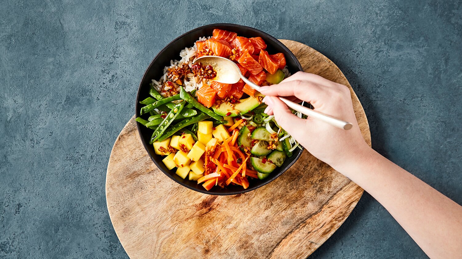 Lakseterninger, mangoterninger, agurkbiter, sukkererter og gulrot over ris.